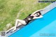 A woman in a black swimsuit laying on the edge of a swimming pool.